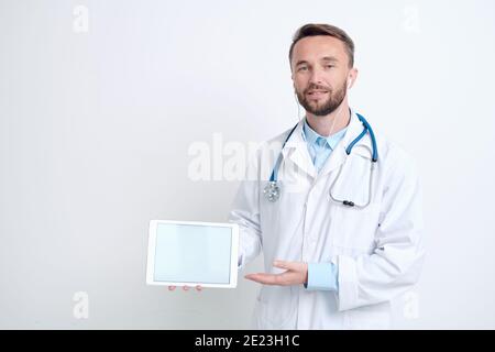 Junge männliche Arzt in Whitecoat, Kopfhörer und Brillen halten digitale Tablette, während die Präsentation der neuen wirksamen Medizin oder Impfstoff Stockfoto