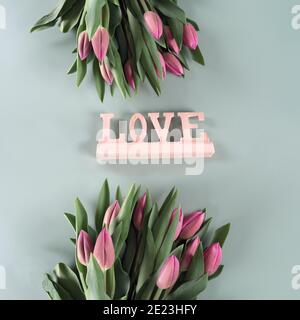 Die Inschrift LIEBE und frische Frühlingsblumen auf grünem Hintergrund, Banner, Frühlingsblumen, rosa Tulpen. Stockfoto