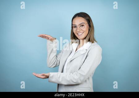 Junge Geschäftsfrau über isolierten blauen Hintergrund gestikuliert mit Händen zeigt große und große Größe Zeichen, Maßnahme Symbol. Lächelnd. Messkonzept. Stockfoto