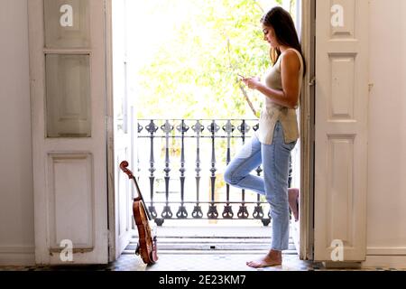 Ein barfuss Mädchen vor einem sonnigen Balkon mit Handy. Stockfoto