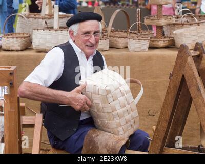 Asturias, Spanien - 4. August 2019 : EIN Handwerker schaut auf die Kamera, während er einen Holzkorb in einem traditionellen Markt macht Stockfoto