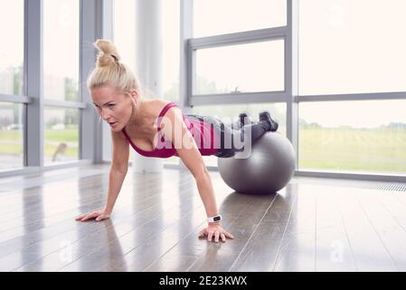 Fokussierte Sportlerin dabei Plank Übung mit Beinen auf Fitness-Ball Im Lichtstudio Stockfoto