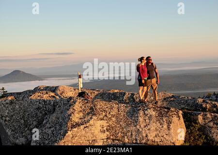 Das Paar umarmt und umarmt sich, nachdem es den Gipfel des Berges erreicht hat Maine Stockfoto