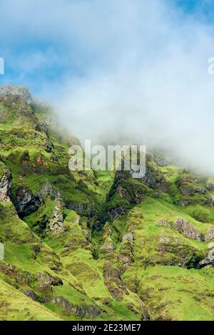 Niedriger Winkel der nebligen Wolke schwebt über entfernten wilden Hang Von Berg mit Gras auf Felsen Stockfoto