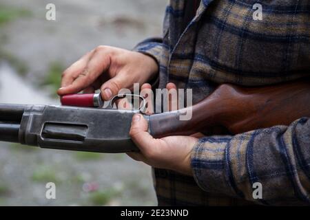 Nahaufnahme eines Mannes, der eine rote Schrotflinte in das Magazin seiner Waffe einlädt. Es hat einen Holzstock gegen die Stahlwirkung. Stockfoto