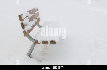 Leere schneebedeckte Bank von der Seite isoliert in Ein gespenstiger Winternebel mit Kopierraum Stockfoto