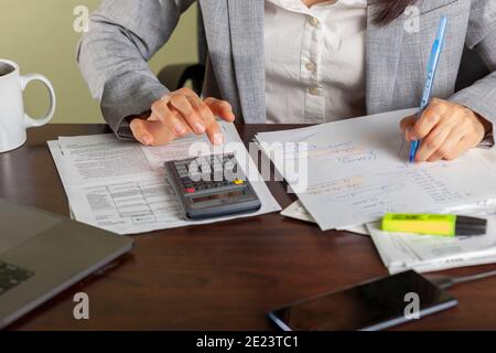 Eine Geschäftsfrau, die formelle Kleidung trägt, arbeitet in einem Büro. Sie berechnet Einkommen und Ausgaben mit Auszügen, Gehaltsabrechnungen, Quittungen ma Stockfoto