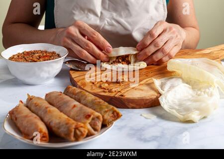 Eine Chefin mit Schürze rollt abgeflachte Kohlblätter Nachdem Sie Reis und Hackfleisch Mischung Füllung in ihnen Um traditionelle Mitte zu machen Stockfoto