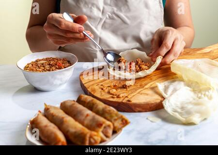 Eine Küchenchefin trägt Schürze setzt Reis und Fleisch Füllung in ein Kohlblatt auf einem Holzbrett. Dann rollt sie es, um traditionelle mittlere Este zu machen Stockfoto