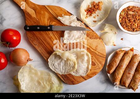 Flaches Bild von Kohlblättern, die auf einem hölzernen Schneidebrett abgeflacht sind, gefüllt mit einer Füllung aus einer Mischung aus Reisfleisch, Tomaten, Zwiebeln und Kräutern Stockfoto