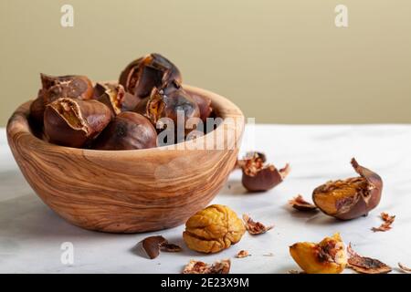Eine Holzschale aus hausgemachten, im Ofen gerösteten Kastanien mit Muscheln und Schalen auf der Marmorplatte verstreut. Ein traditioneller Winter-, Herbst-Snack mit Stockfoto