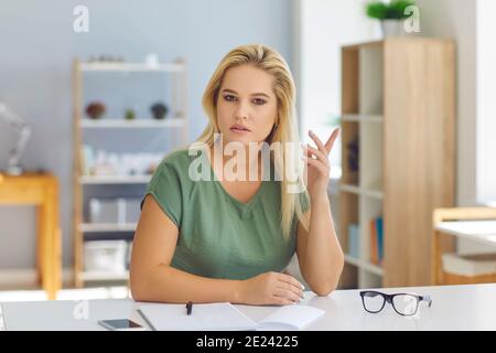 Seriöse junge Frau, die am Schreibtisch sitzt, Arbeitsfragen diskutiert und ihre Meinung teilt Stockfoto