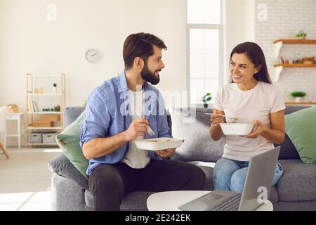 Verheiratetes Paar, das sich mit dem Takeaway Tablett mit Essen unterhielt und zu Hause auf dem Sofa saß. Stockfoto