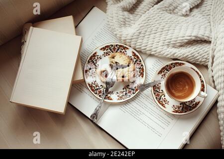 CORK, IRLAND - 01. Jan 2021: Ein Weihnachtskuchen und eine Tasse Kaffee in Vintage-Tee Delph auf einem offenen Buch neben gemütlicher Decke und Bücher mit Kopie sp Stockfoto