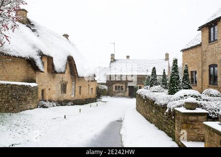 Cotswold Stein Reetgedeckten Hütte und Häuser entlang einer Straße im Schnee zu Weihnachten. Taynton, Cotswolds, Oxfordshire, England Stockfoto