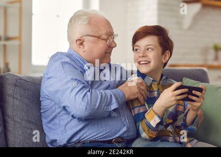 Glücklicher Enkel und Großvater sitzen auf dem Sofa und spielen Auf einem neuen Mobiltelefon Stockfoto