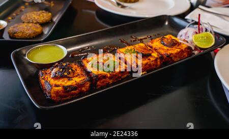 Selektiver Fokus von Paneer Tikka Kebab serviert mit grünem Chutney auf einem schwarzen Serviertablett Stockfoto