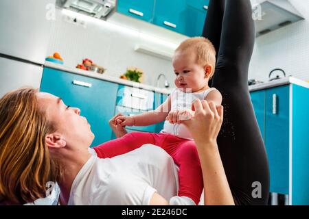 Eine Mutter mit ihrem Baby macht Fitness in der Küche. Ansicht von unten. Das Konzept des Heimsporttrainings mit Kindern. Stockfoto