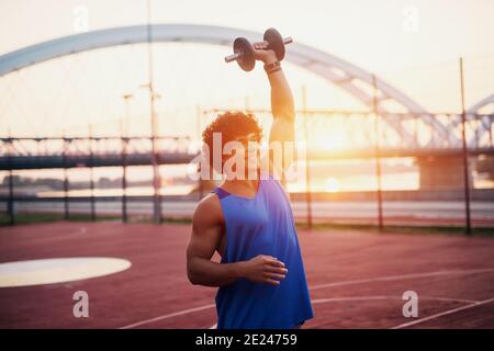 Junge sportliche fit Mann hält Gewicht in seinem Arm. Außerhalb des frühen Morgentrainings. Stockfoto