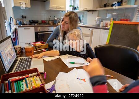 Ein drei Jahre altes Mädchen zu Hause lernen mit ihrer Mutter mit einem Laptop auf dem Küchentisch. Stockfoto