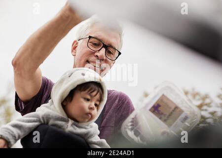 Lächelnder reifer Mann mit Baby, der Müll in den Papierkorb legt Stockfoto