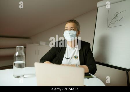 Frau trägt Gesichtsmaske vor dem Laptop Stockfoto