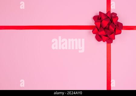 Flache Lay-Komposition mit dekorativer roter Schleife auf rosa Hintergrund mit Platz für Text. Geben präsentiert Konzept. Grußkarte oder Feiertage Stockfoto