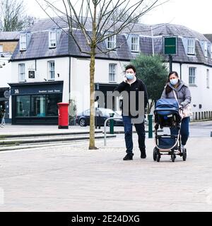 London Großbritannien, junger asiatischer Mann Frau Familienpaar schieben EIN Kind in EINEM Buggy entlang einer leeren High Street Tragen von Schutzgesichtenmasken während covid-19 Loc Stockfoto