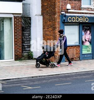 London Großbritannien, junger Mann oder Vater allein schieben EIN Baby oder Kind in EINEM Kinderwagen entlang einer leeren High Street während Covid-19 Pandemic Lockdown Stockfoto