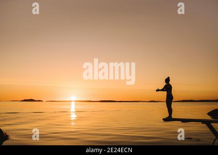 Silhouette einer Frau, die auf dem Sprungbrett auf See steht Stockfoto