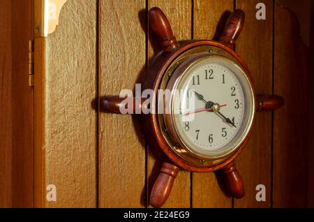 Wanduhr in Form von Schiffsruder. Die Uhr im nautischen Stil ist an einer Holzkiste befestigt. Selektiver Fokus. Stockfoto