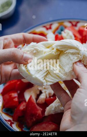 Hand zerbröckeln eine Mozzarella Käseball über einige Tomaten. Caprese Salat Stockfoto