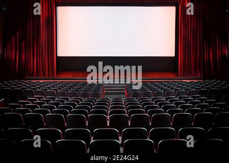 Auditorium eines leeren Kinos und Bühne mit geöffnet Rote Samtvorhänge von der Rückseite der Reihen betrachtet Sitze mit Beleuchtung auf dem Bildschirm Stockfoto