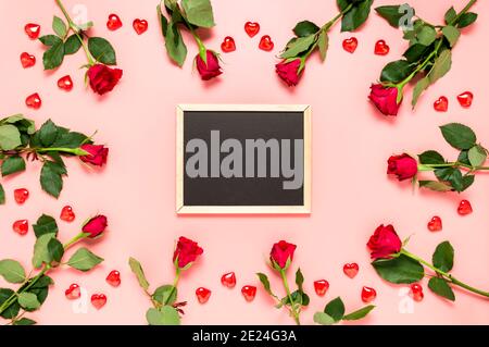 Leere Tafel mit roten Rosen und Herzen auf rosa Valentinstag Hintergrund umgeben. Geburtstag, Muttertag, Frauentag oder Hochzeitsfeier. Begrüßung Stockfoto