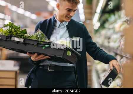 Mann, der in einem Supermarkt in der Produktion arbeitet. Mann, der das Regal mit frischen Produkten auffüllt. Stockfoto