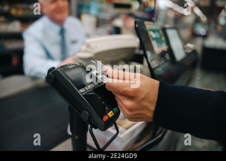 Nahaufnahme eines männlichen Kunden, der eine kontaktlose Zahlung mit seiner Kreditkarte im Lebensmittelgeschäft macht. Der Käufer zahlt für seinen Einkauf mit einer Kreditkarte. Stockfoto