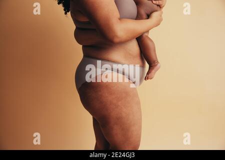 Seitenansicht einer Mutter, die ihr Baby trägt und vor braunem Hintergrund steht. Gesunde Frau mit Baby. Stockfoto