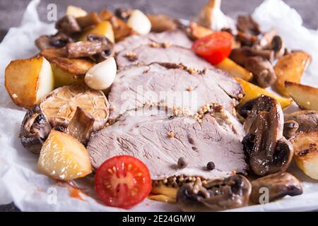 Scheiben gebratenes Fleisch. Kaltgekochtes Schweinefleisch mit Pilzen, Kartoffeln, Knoblauch und Kirschtomaten auf Pergament. Stockfoto