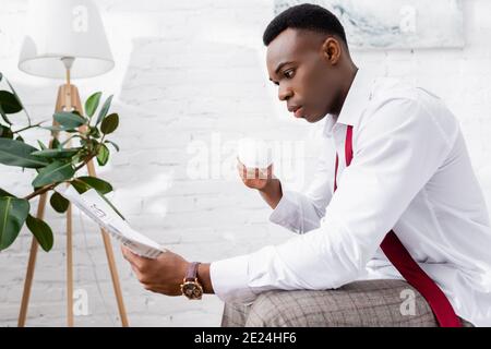 afroamerikanischer Geschäftsmann liest Zeitung und hält eine Tasse Kaffee Zu Hause Stockfoto