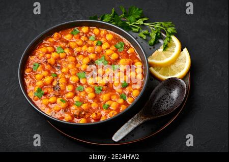 Chana Masala oder Chole in schwarzer Schale auf dunkler Schieferplatte. Indische Küche Gemüse Kichererbsen Currygericht. Asiatische würzige vegetarische Speisen und Gerichte. Stockfoto