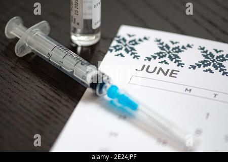 Nahaufnahme einer medizinischen Spritze auf einem Juni-Kalender mit einem Impfstofffläschchen im Hintergrund platziert, symbolisiert geplante Impfung, Gesundheitsplanung Stockfoto