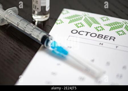 Nahaufnahme einer medizinischen Spritze auf einem Oktober-Kalender mit einer Impfstoffflasche im Hintergrund, die die geplante Impfung symbolisiert Stockfoto