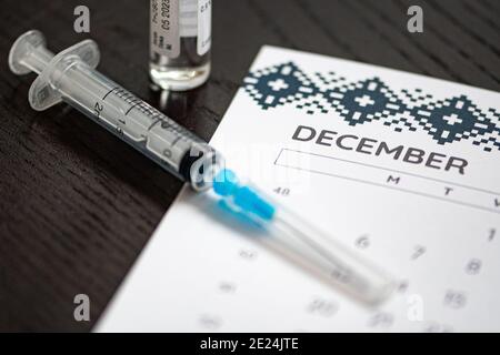Nahaufnahme einer medizinischen Spritze auf einem Dezemberkalender mit einer Impfstoffflasche im Hintergrund, die die geplante Impfung symbolisiert Stockfoto