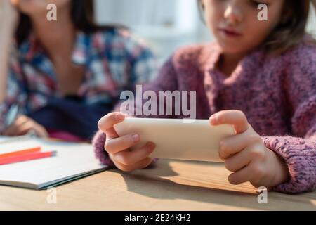 Beschnittene Ansicht der Tochter mit Smartphone in der Nähe der Mutter am Schreibtisch Auf unscharfem Hintergrund Stockfoto