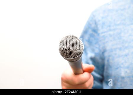 Ein Mann hält ein silbernes, graues Mikrofon in der Hand und führt Geschäftsinterviews, journalistische Berichterstattung, Public Speaking, Pressekonferenz, Karaoke Stockfoto