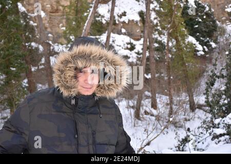 Schneetag, Mann mit Militärjacke und Kapuze, der die Kamera anschaut. Szene nach dem Schneesturm namens Filomena in Spanien. Januar 2021. Stockfoto