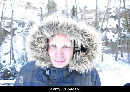 Porträt des Mannes ohne Bart mit Kapuze mit Haaren in verschneiten Bereich. Szene nach dem Schneesturm namens Filomena in Spanien. Januar 2021. Stockfoto