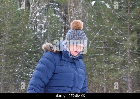 Pensionierte Frau in Jacke und Hut mit bunten Farben Blick in einen Pinienwald von Schnee bedeckt. Szene nach dem Schneesturm namens Filomena in Stockfoto