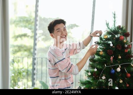 Mann, der Weihnachtsdekoration zu Hause mit einer Kugel aufstellt In seiner Hand Stockfoto