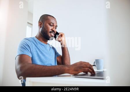 Ein Mann nimmt einen Geschäftsanruf an, während er einen Laptop benutzt Stockfoto